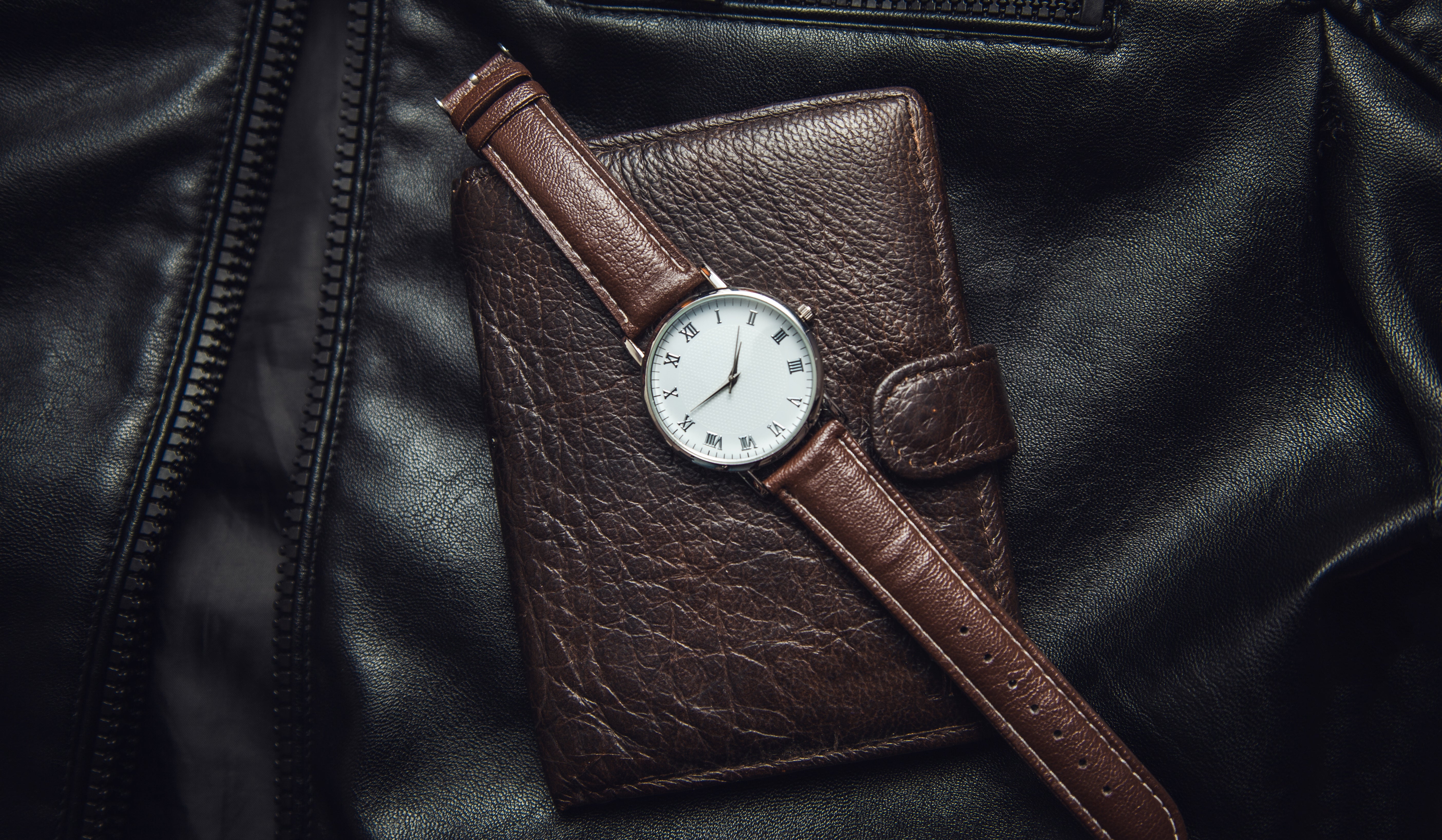 Jolie montre vintage marron en cuir, posée sur un portefeuille également marron en cuir et sur une veste en cuir noire.